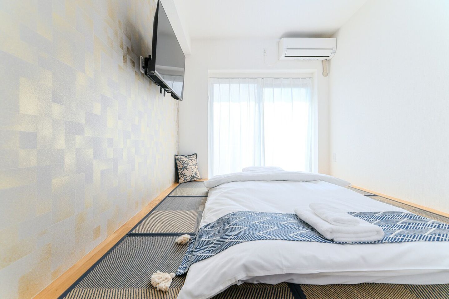 Japanese futon bed on tatami mats in a bright room with a wall-mounted TV.