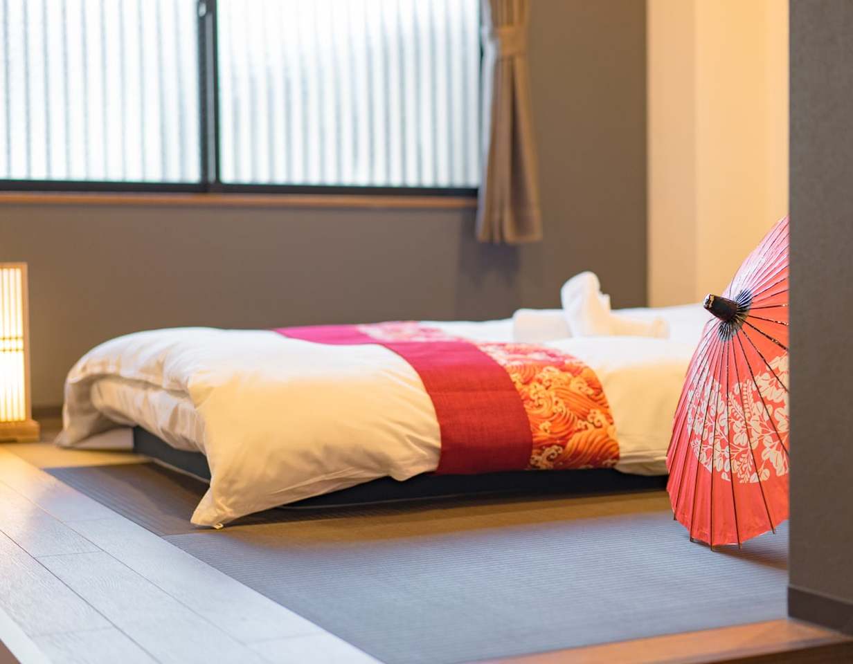 A Japanese-style futon bed on tatami mats with a decorative red paper umbrella.