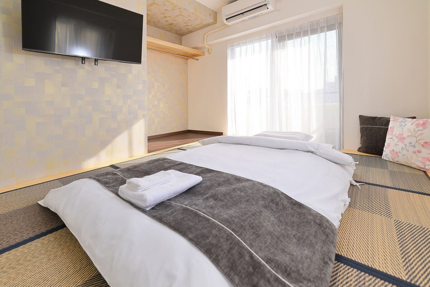 Japanese futon bed on tatami mats in a modern bedroom with a wall-mounted TV.