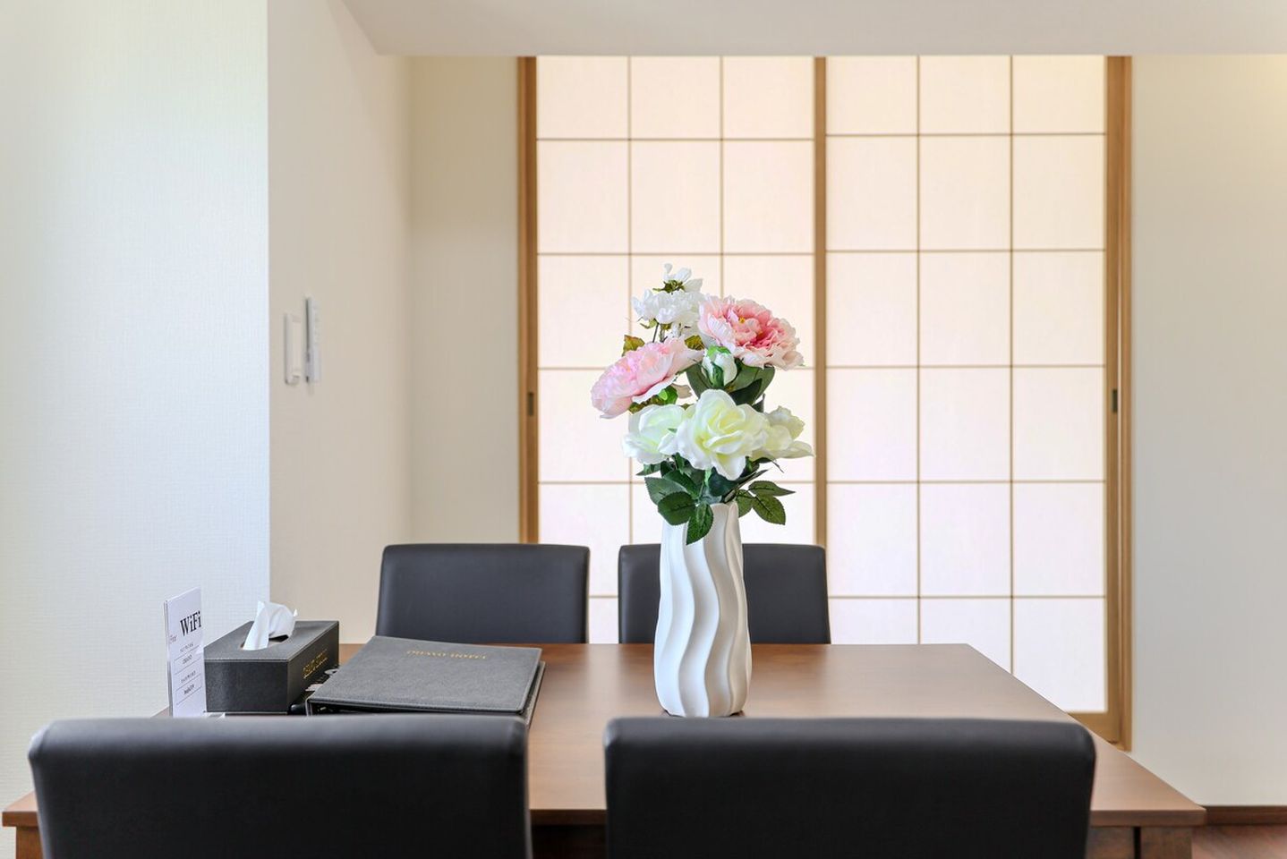 Wooden dining table with black chairs, a flower vase centerpiece, and shoji screen doors in the background.