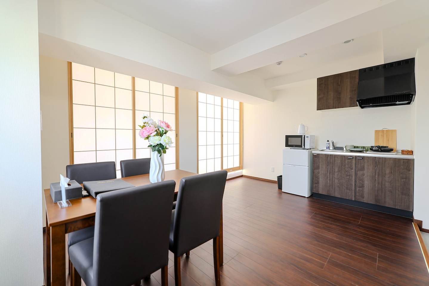 Dining table with chairs next to a small kitchen with dark wood cabinets and traditional shoji screens.