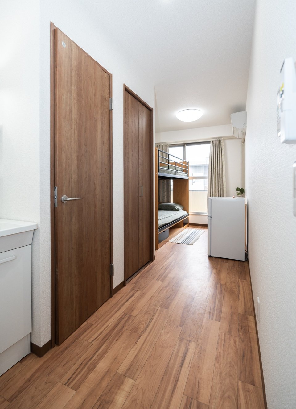 Hallway with wooden doors leading to a studio apartment with a bunk bed and a small refrigerator.
