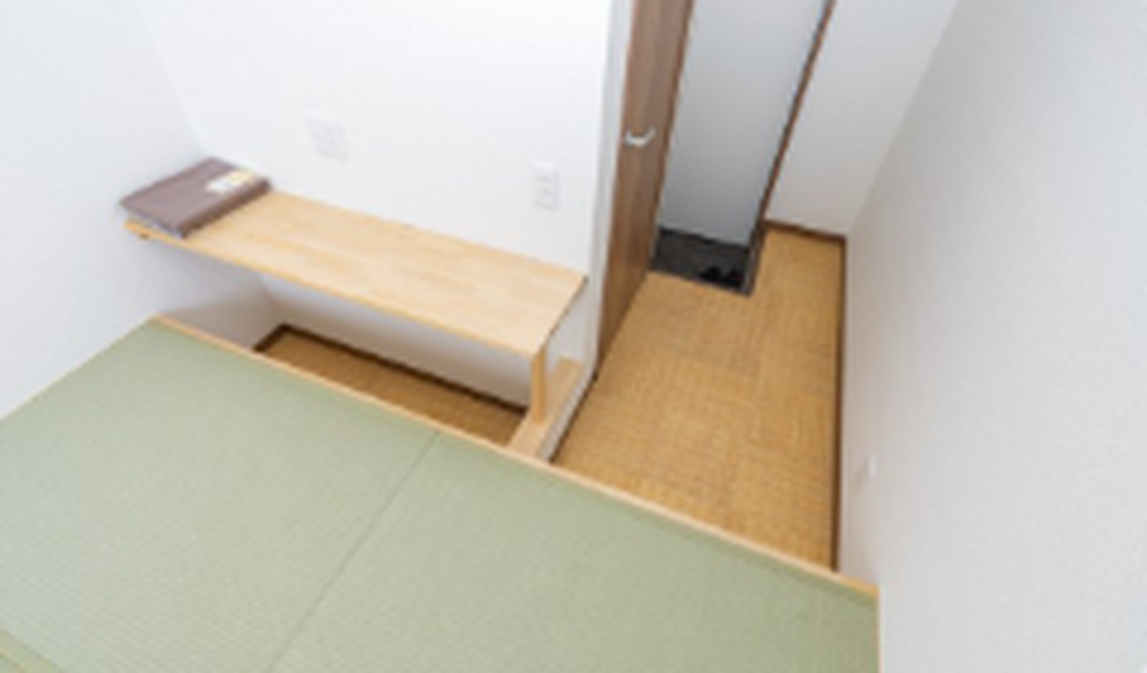 Japanese-style room with green tatami mats, a wooden wall shelf, and light-colored walls.