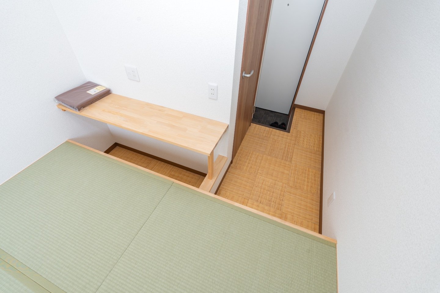 Raised tatami mat sleeping area with a wooden shelf next to an entryway.