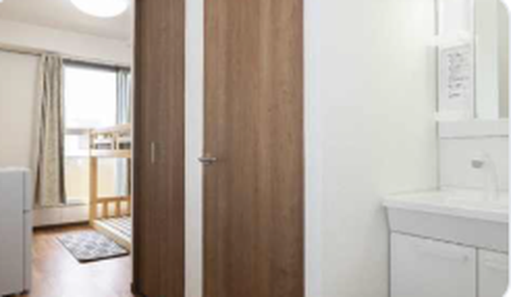 A hallway with a white vanity sink, wooden doors, and a view of a bedroom with a bunk bed.