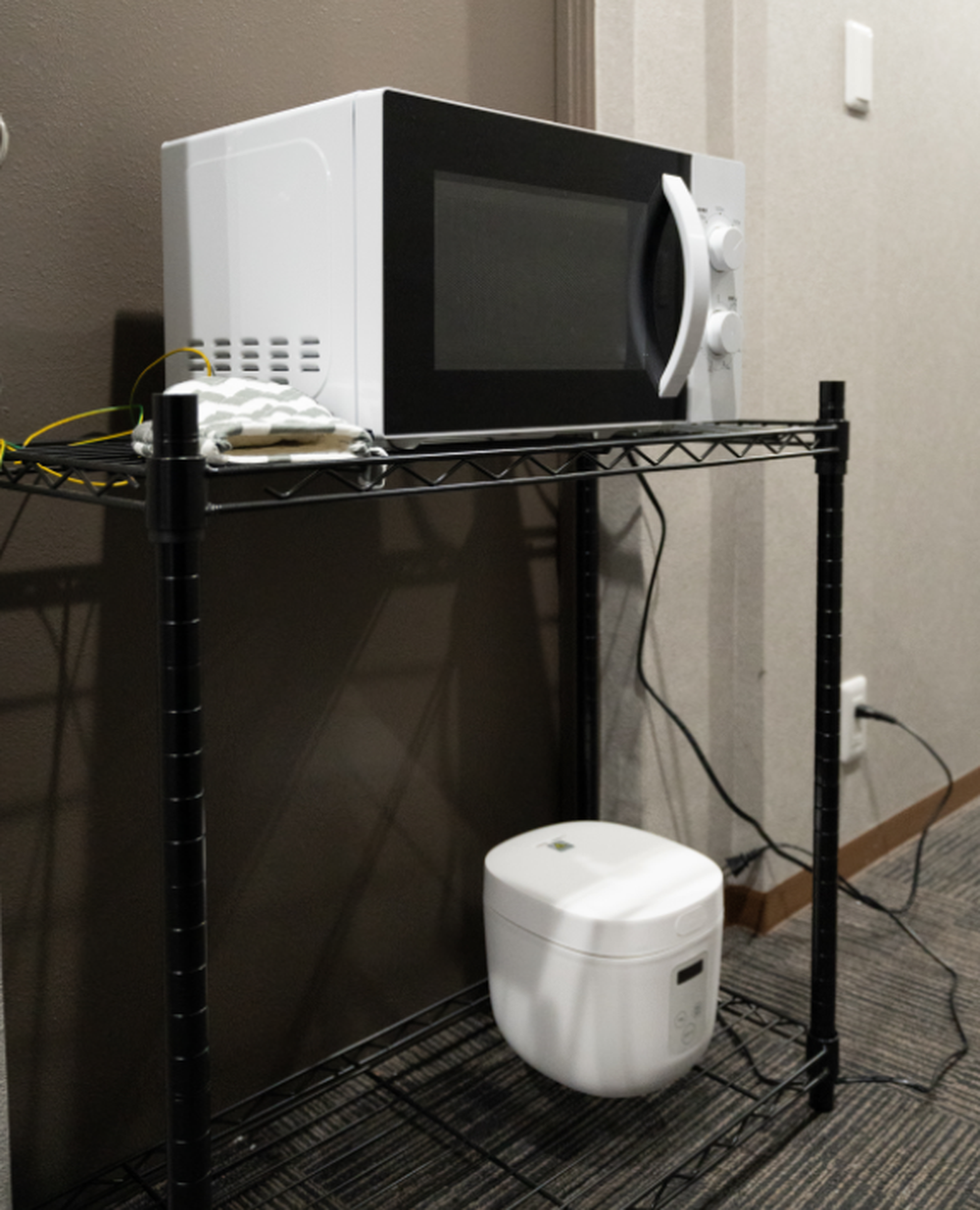 White microwave and rice cooker on a black wire storage rack.