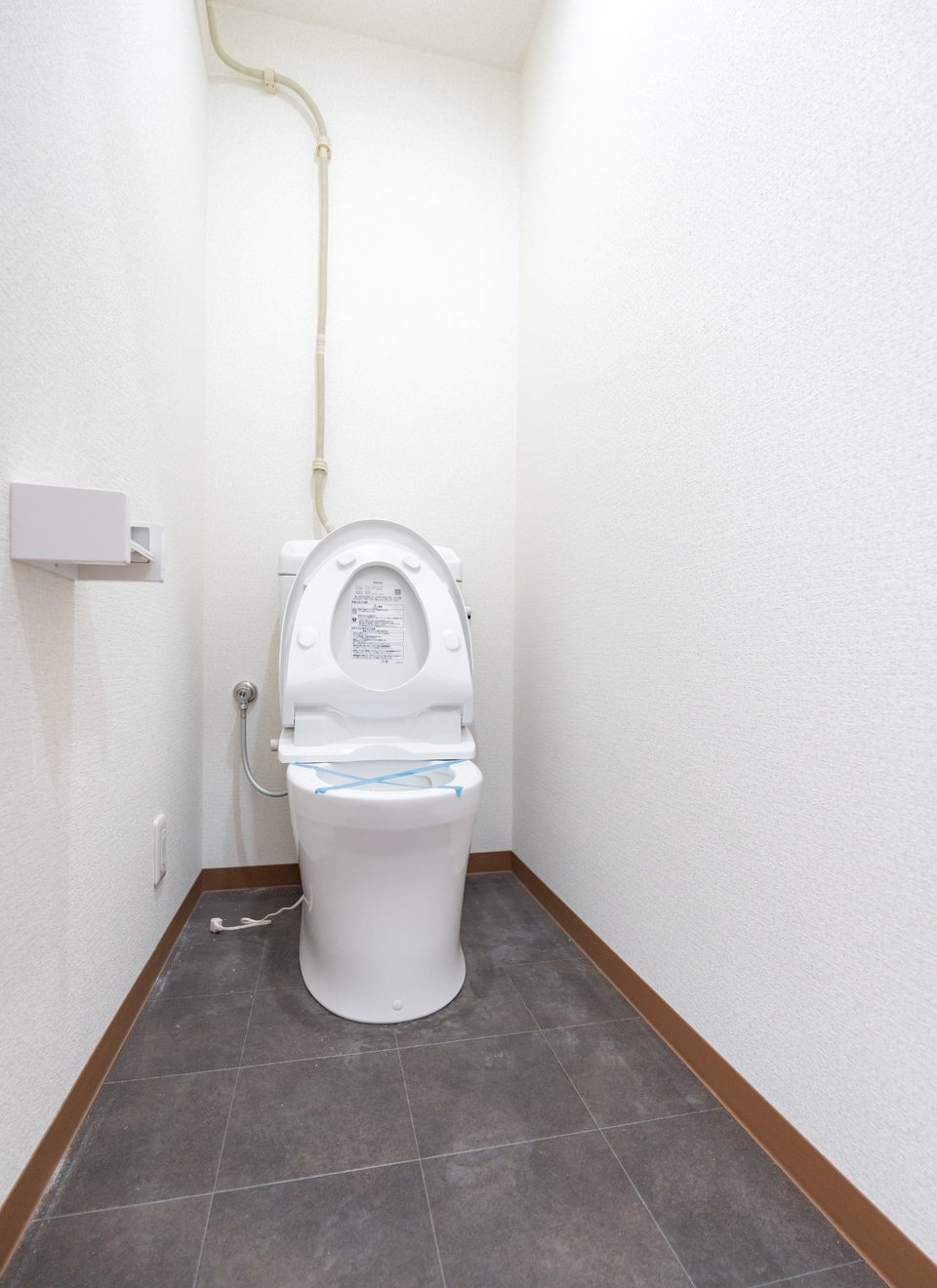 A clean white toilet with an open lid in a narrow restroom with dark tiled flooring.
