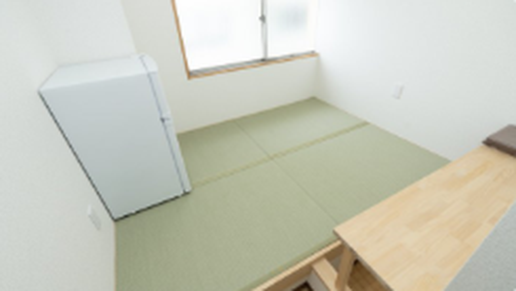 Small Japanese-style room with green tatami mats, a white refrigerator, and a wooden table.