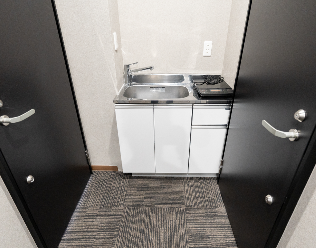 Compact kitchenette with a stainless steel sink and portable induction cooktop between two black doors.