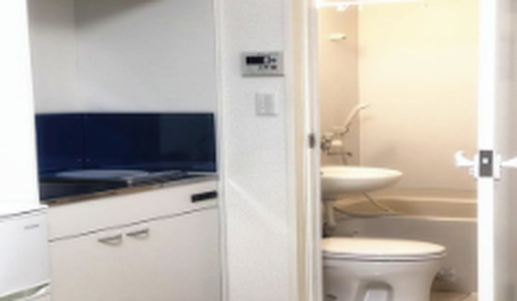 A view of a compact kitchen counter next to an open bathroom door showing a toilet, sink, and bathtub.