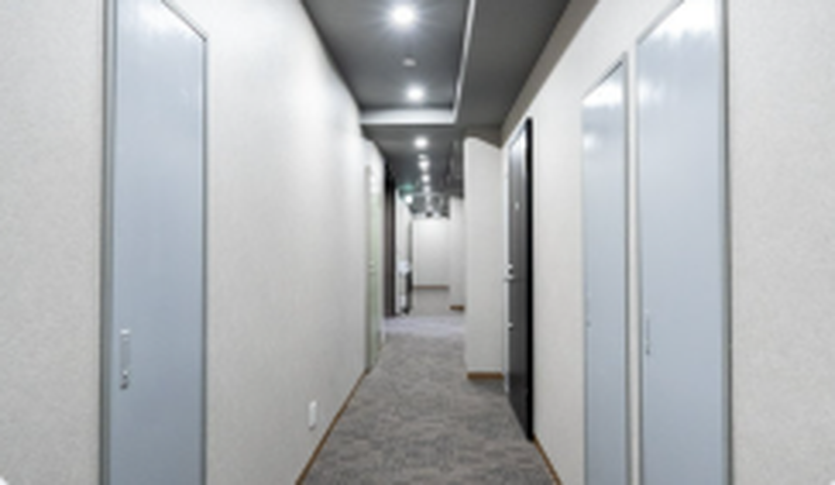 A long carpeted building hallway with recessed ceiling lights and doors on both sides.