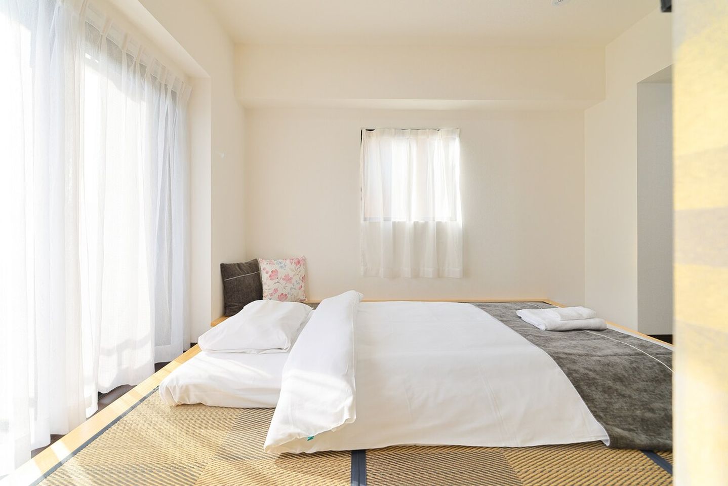 Futon bedding laid on tatami mats in a bright minimalist bedroom with sheer white curtains.