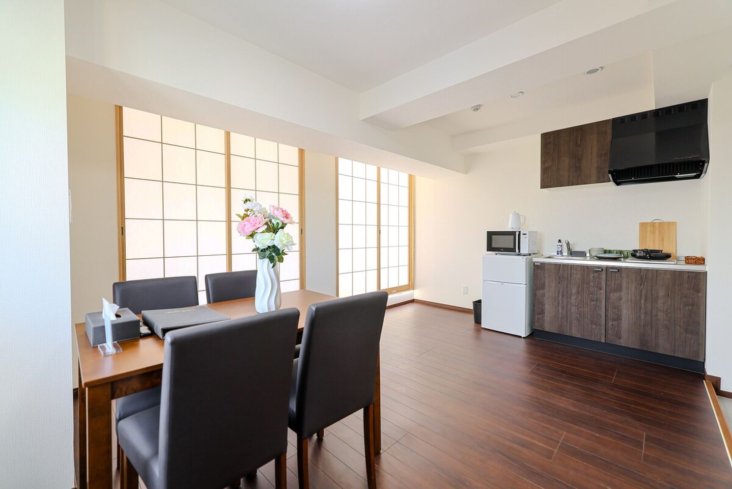 Dining table with chairs next to a compact kitchen with dark wood cabinets and shoji screen windows.