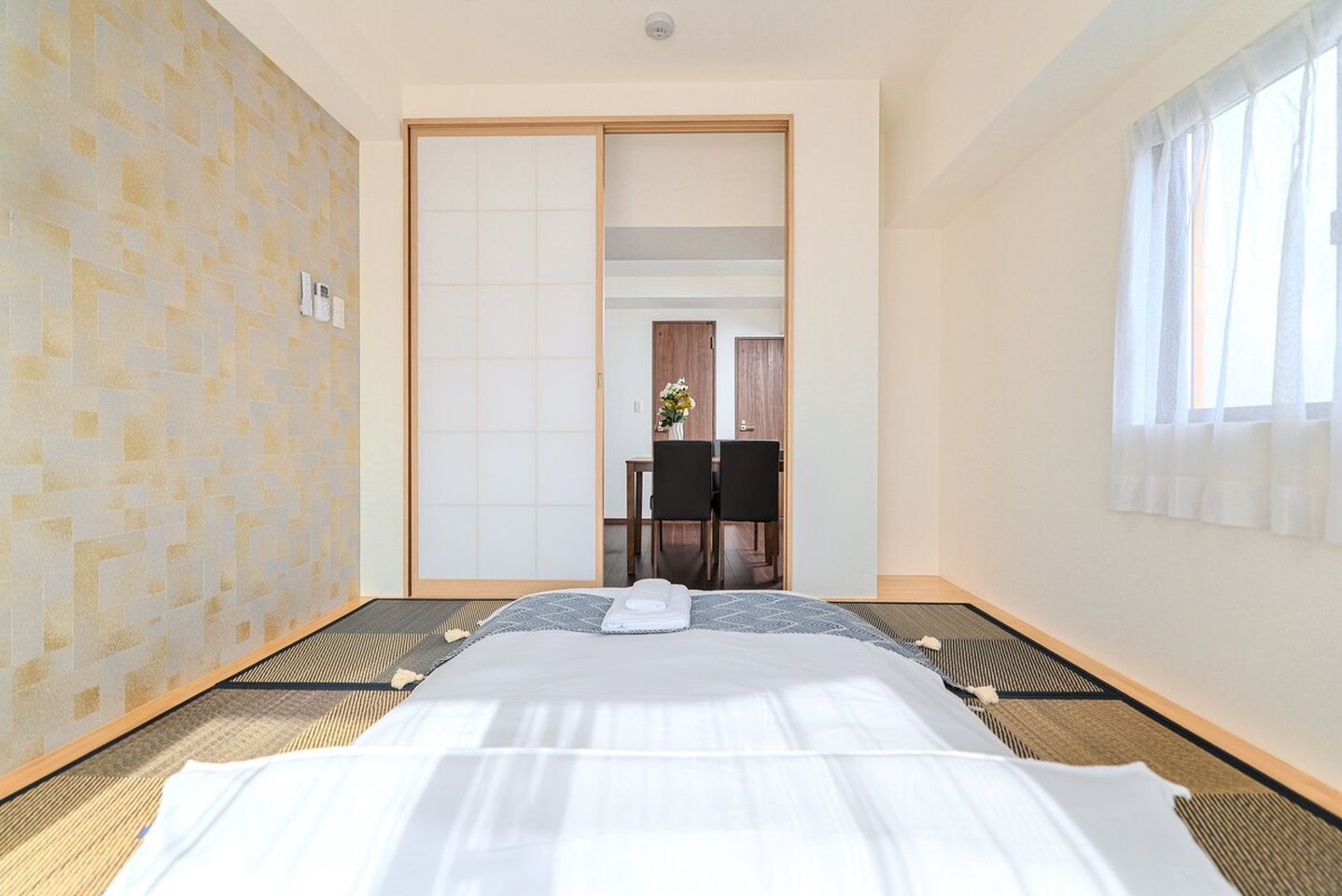 Futon laid on tatami mats in a Japanese-style bedroom with sliding doors opening to a dining room.